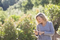 Mulher em suéter usando telefone no jardim ensolarado — Fotografia de Stock