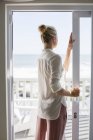 Junge Frau steht am Fenster in Haus an der Küste — Stockfoto