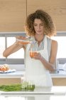 Woman pouring vegetable juice into glass in kitchen — Stock Photo