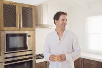 Homem segurando vidro de suco na cozinha e sorrindo — Fotografia de Stock