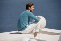 Молодий розслаблений чоловік сидить на терасі на березі озера — стокове фото
