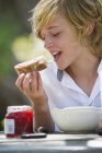 Хлопчик-підліток з білявим волоссям їсть хліб з джемом на відкритому повітрі — стокове фото