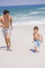 Homme joyeux courir avec son fils sur la plage de sable fin — Photo de stock