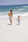 Веселый мужчина бегает с сыном на песчаном пляже — стоковое фото