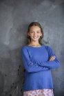 Retrato de menina sorridente com os braços cruzados em pé na frente do quadro negro em sala de aula — Fotografia de Stock