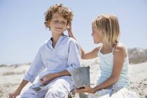 Girl holding shell next to brother ear on beach — Stock Photo