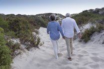 Happy senior couple walking on sandy beach at sunset — Stock Photo