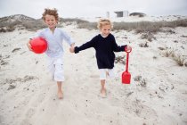 Niños sosteniendo juguetes y corriendo sobre arena - foto de stock