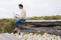 Mann sitzt auf Uferpromenade in der Natur und liest Zeitung — Stockfoto