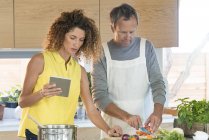Casal preparando alimentos na cozinha com tablet digital — Fotografia de Stock