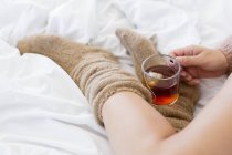 Primer plano de la mujer con taza de té de hierbas en la cama - foto de stock