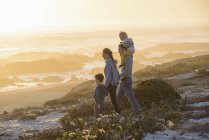 Felice giovane famiglia a piedi sulla spiaggia al tramonto luminoso — Foto stock