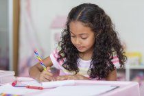 Focused little girl doing homework at table — Stock Photo