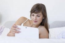 Молодая женщина лежит на кровати и с помощью цифрового планшета — стоковое фото