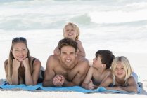 Retrato de familia feliz acostada sobre una manta en la playa - foto de stock