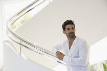 Thoughtful man standing on staircase in modern house — Stock Photo