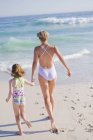 Жінка біжить на піщаному пляжі з дочкою — стокове фото