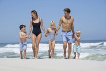 Felice famiglia che cammina sulla spiaggia tenendosi per mano — Foto stock