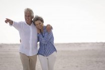 Happy embracing senior couple walking on beach — Stock Photo