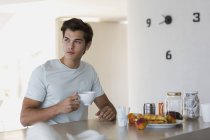 Крупним планом вдумливий молодий чоловік п'є каву за столом на кухні — стокове фото