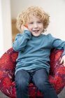 Мальчик разговаривает по мобильному телефону в кресле дома — стоковое фото