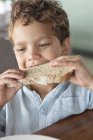 Gros plan du petit garçon qui mange du pain sur fond flou — Photo de stock