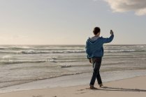 Young man using mobile phone while walking on beach — Stock Photo