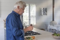 Uomo anziano che prepara verdure in cucina — Foto stock