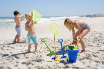 Tres niños jugando en la playa - foto de stock