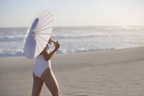 Frau im Badeanzug mit Sonnenschirm spaziert am Sandstrand — Stockfoto