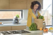 Woman taking out food from paper bag in kitchen — Stock Photo