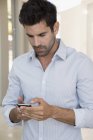 Nachdenklicher Mann im weißen Hemd bedient Smartphone — Stockfoto