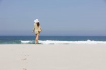 Vista posteriore della donna in cappello in piedi sulla spiaggia sabbiosa — Foto stock