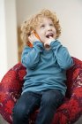Мальчик разговаривает по мобильному телефону с пальцем во рту в кресле — стоковое фото