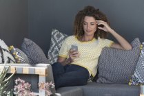 Donna seduta sul divano a casa e utilizzando smartphone — Foto stock