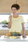 Portrait of young woman holding slice of pineapple in kitchen — Stock Photo