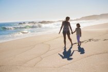 Mujer caminando en la playa con su hija - foto de stock