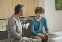 Father talking to son using digital tablet in living room — Stock Photo