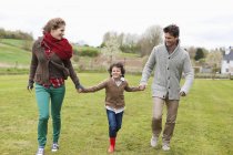 Famille heureuse marchant dans un champ vert — Photo de stock