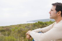 Вдумчивый человек сидит на берегу и смотрит на море — стоковое фото