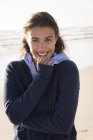 Ritratto di giovane donna affascinante in calda felpa con cappuccio in piedi sulla spiaggia — Foto stock