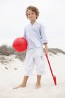 Garçon tenant pelle jouet et balle sur la plage de sable — Photo de stock