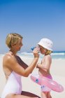 Donna che si mette gli occhiali da sole sulla faccia figlia sulla spiaggia — Foto stock