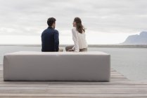 Rückansicht eines Paares, das auf einem Hocker am See sitzt und die Aussicht betrachtet — Stockfoto