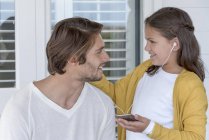 Happy father with little daughter listening to music on mobile phone with earbuds — Stock Photo