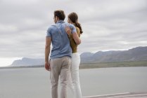 Young embracing couple standing at lake shore — Stock Photo