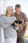 Sourire couple d'âge mûr en utilisant une tablette numérique à l'extérieur — Photo de stock