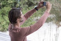 Молодой человек делает селфи с мобильного телефона в саду — стоковое фото