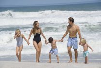 Glückliche Familie, die Händchen haltend am Strand spaziert — Stockfoto