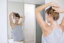Young woman adjusting hair in front of mirror in bathroom — Stock Photo